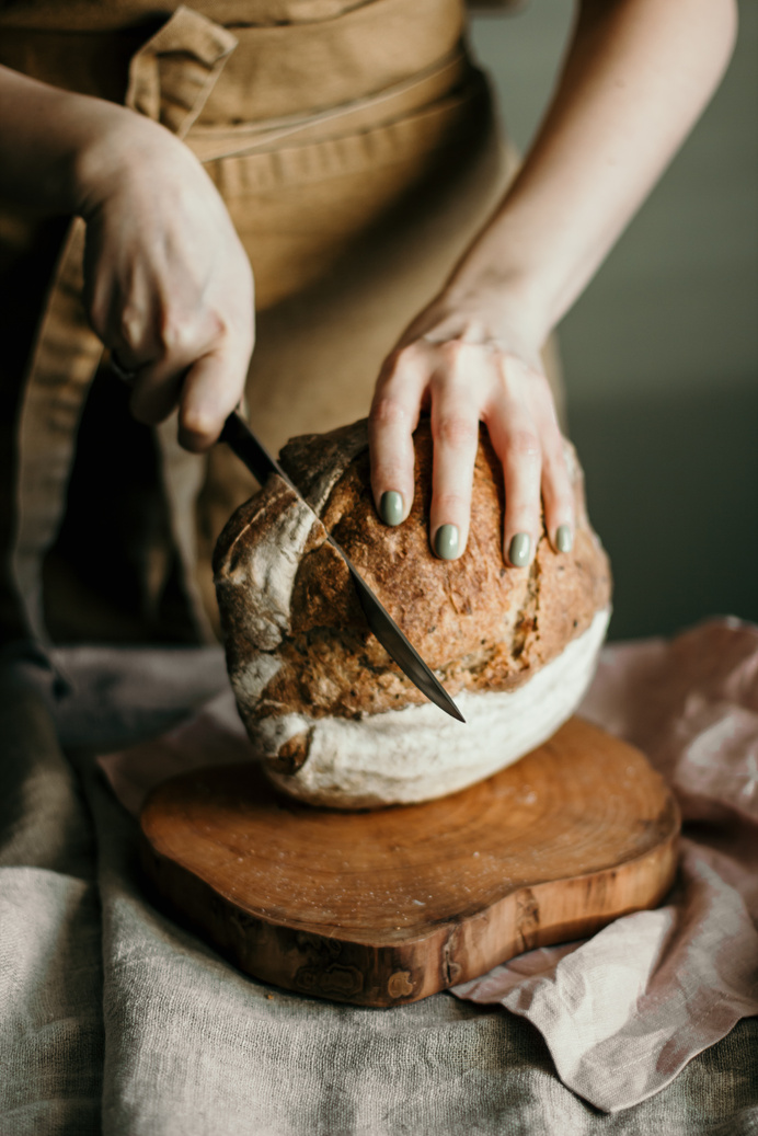 Woman cutting sourdough bread on wooden cutting board